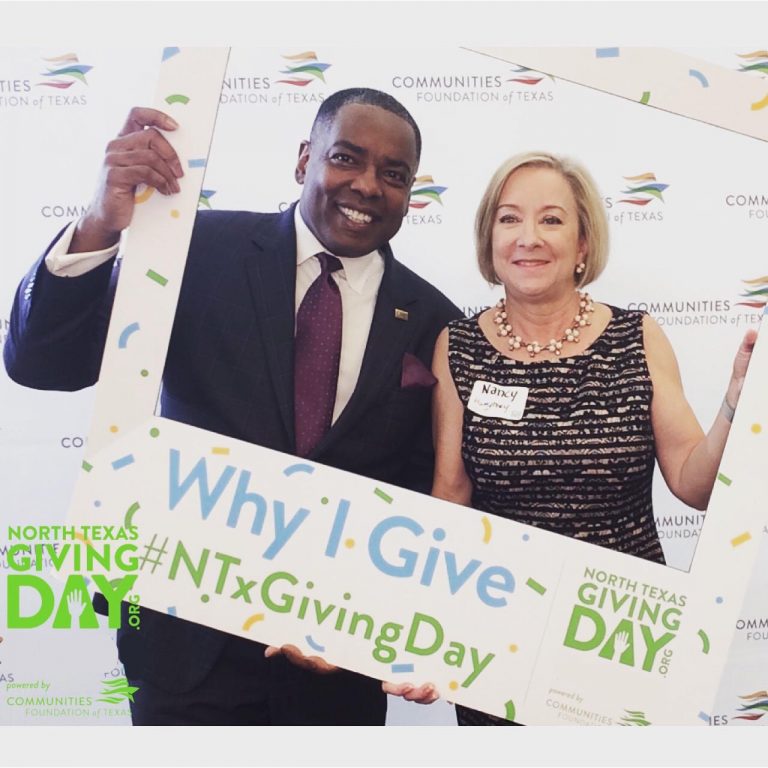 Man and woman peaking through large photo frame for North Texas Giving Day